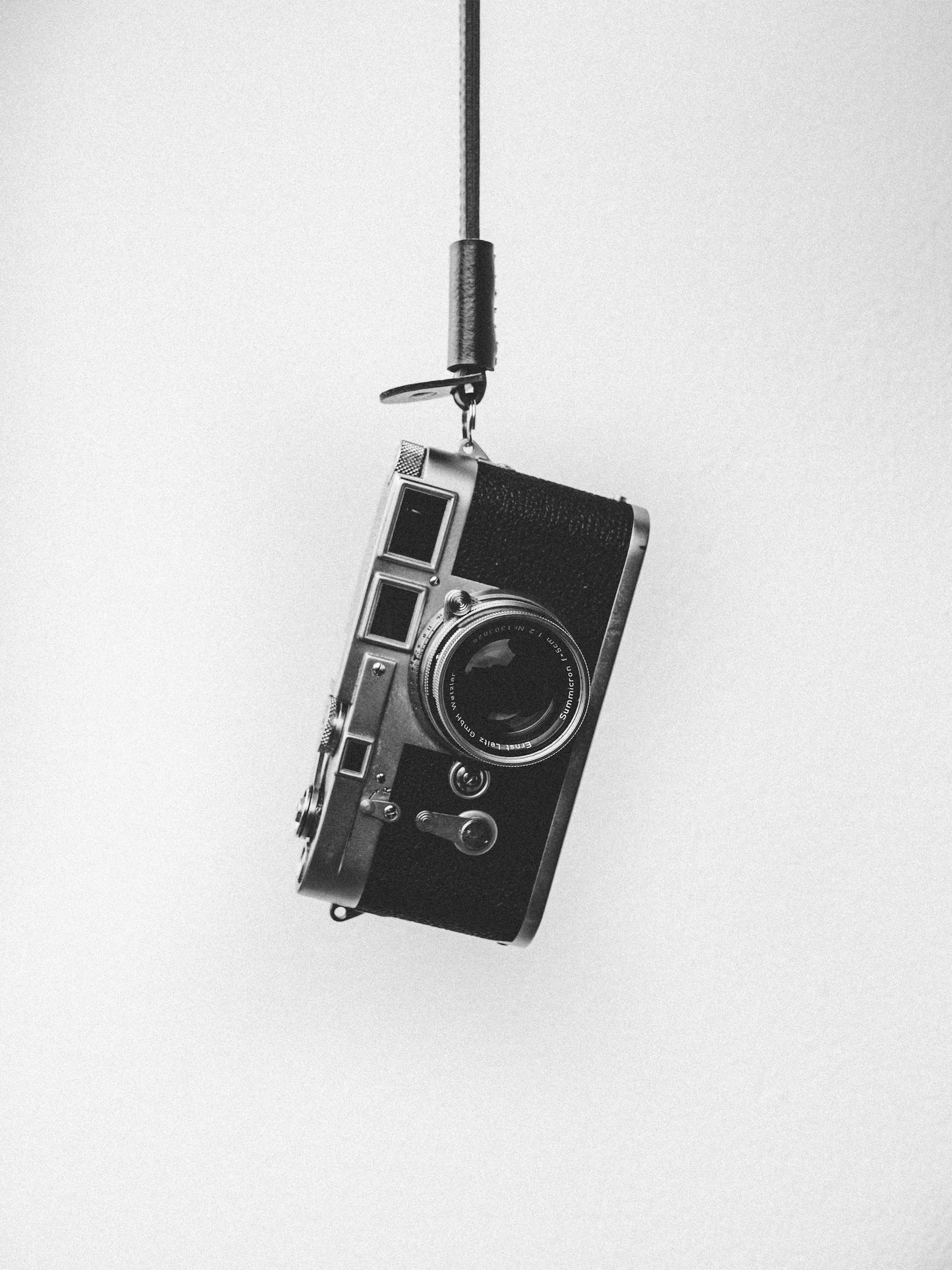 A vintage camera hanging from a ceiling cord against a plain background.