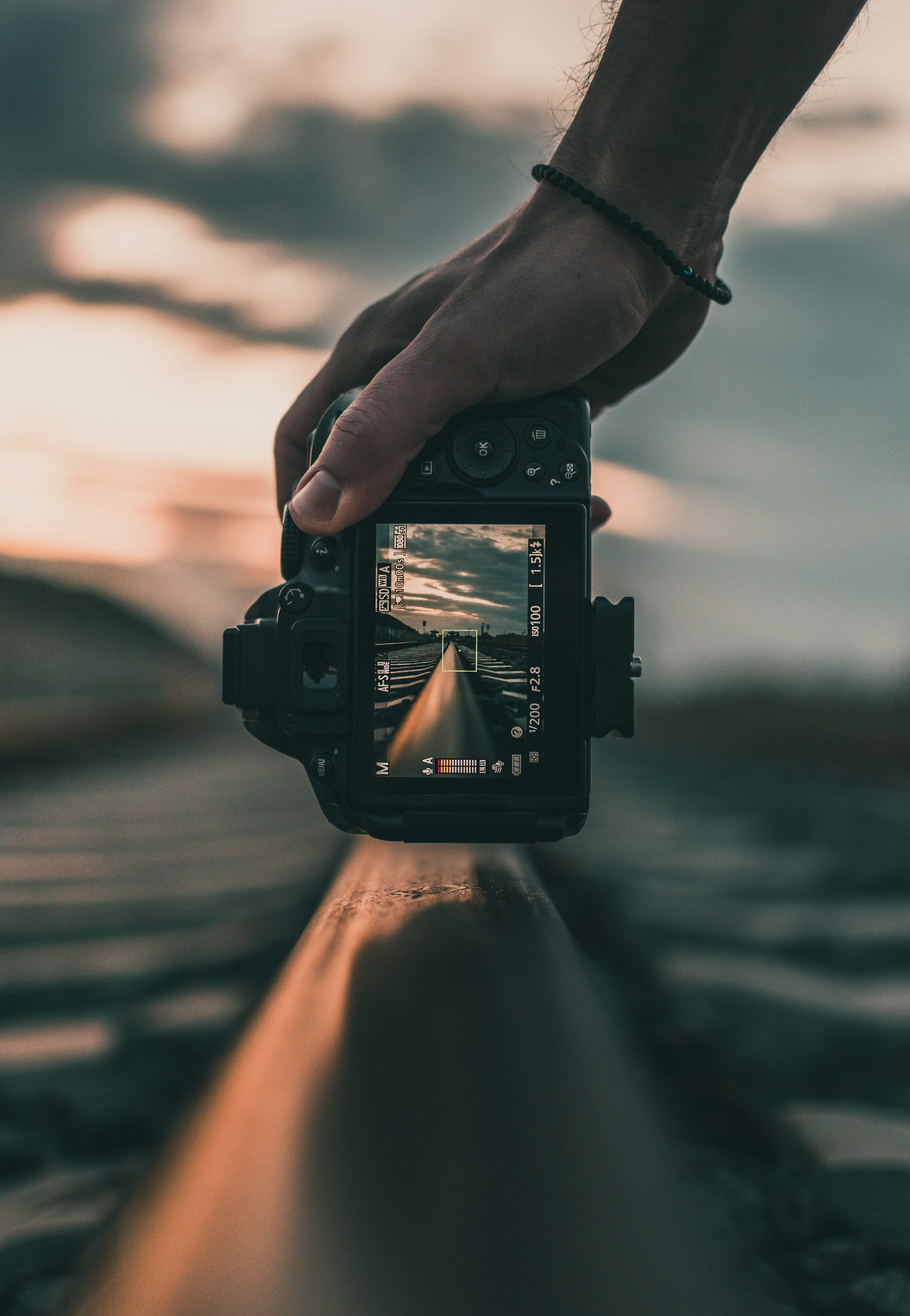 A person holding a camera captures a road view at sunset or sunrise, with the camera's screen showing a straight empty road with sky and clouds.