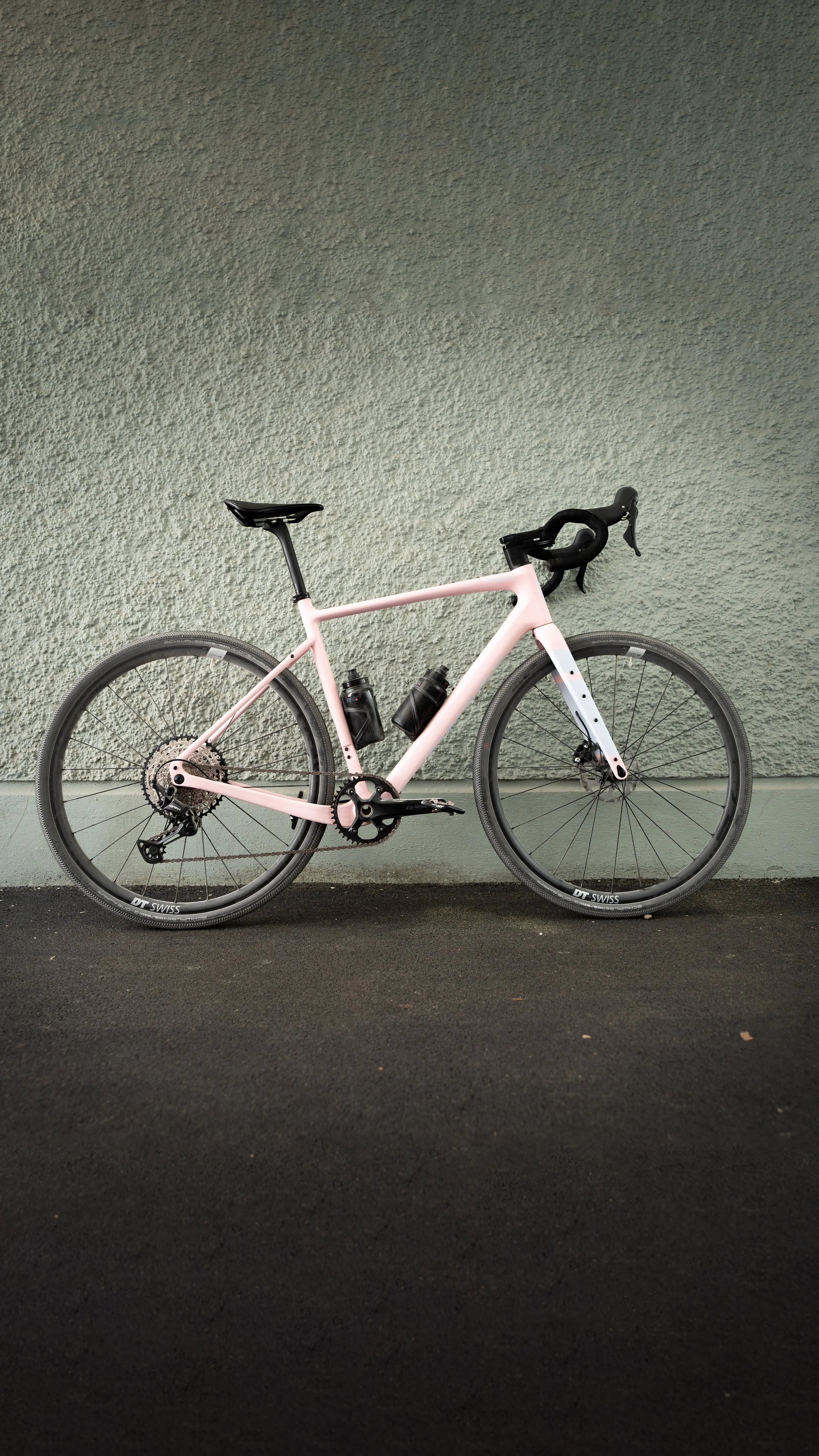 Ein rosa Fahrrad mit schwarzen Reifen steht vor einer grauen Wand.