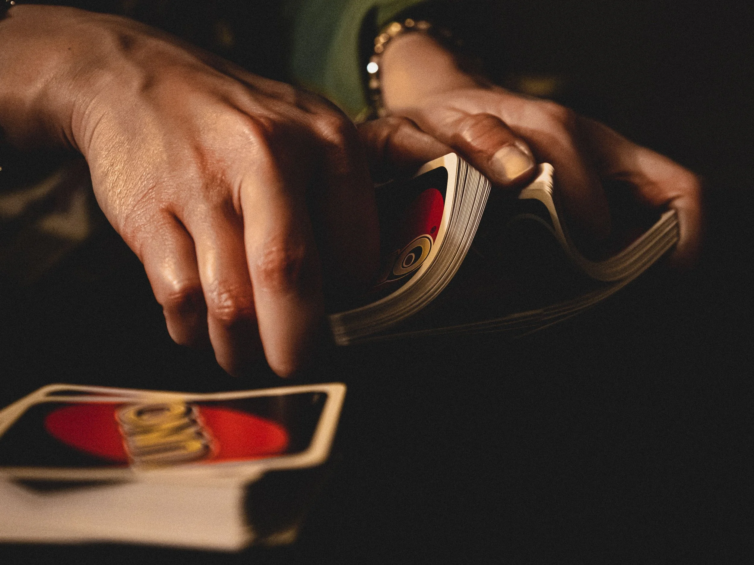 Close-up of hands holding a deck of playing cards, with a focus on the top card which is the King of Hearts, on a dark background.