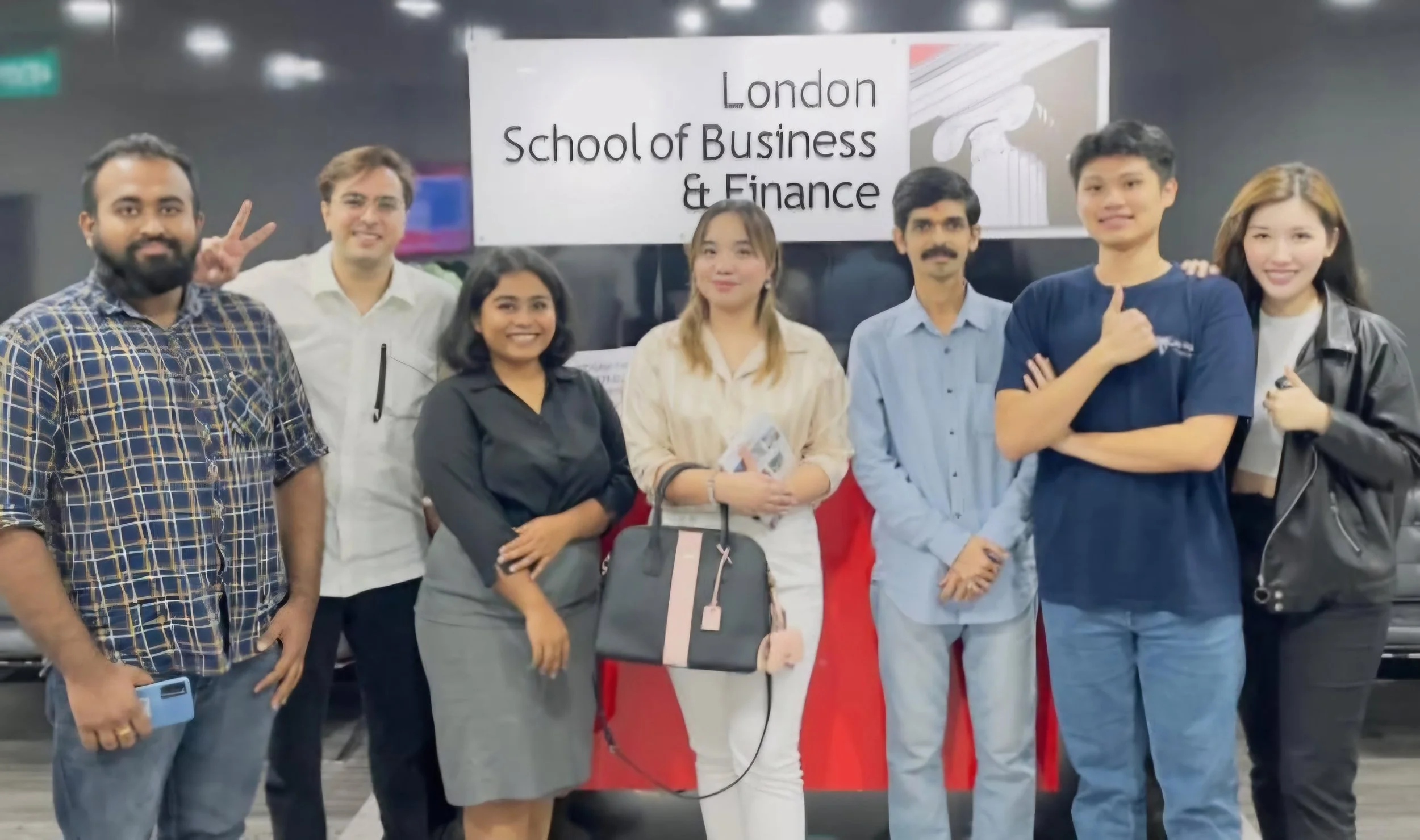 Group of students posing in front of a sign that reads 'London School of Business & Finance' at an indoor location, some smiling and making peace signs.