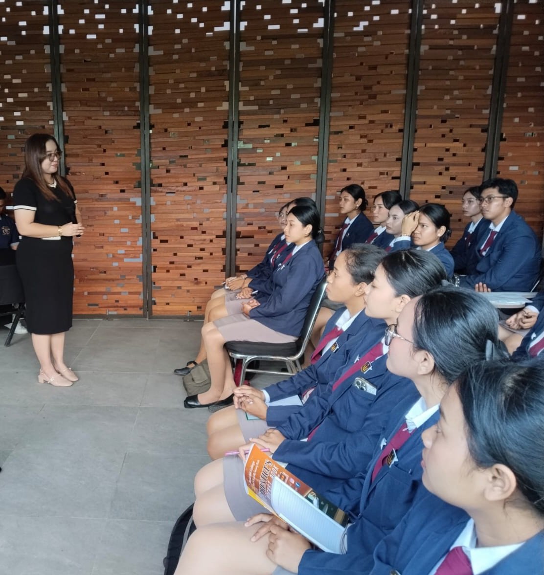 A woman in black clothing giving a presentation to a group of students in uniforms seated and listening attentively.