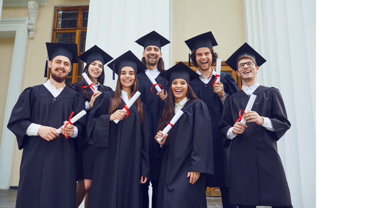 Group of young adults in graduation gowns and caps holding diplomas and smiling outside a building.