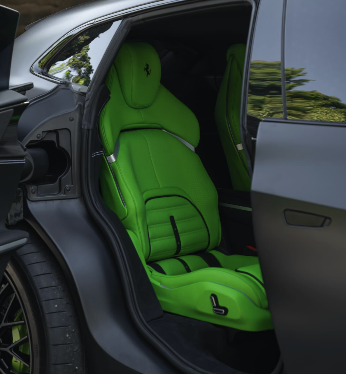 Inside of a luxury sports car with bright green leather seats and headrests, featuring a Ferrari logo, seen through an open door showing a sleek black exterior.
