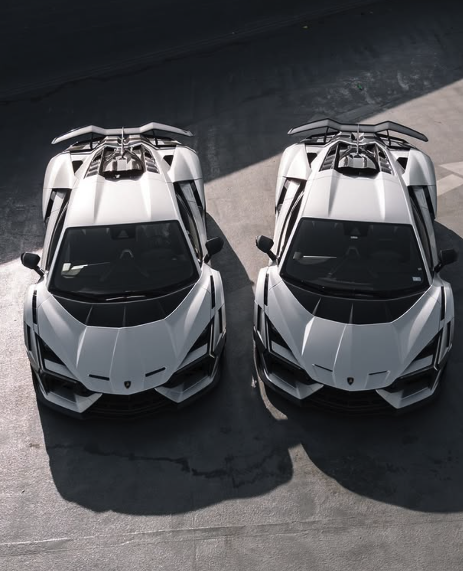Two white luxury sports cars parked side by side on a dark asphalt surface, viewed from above.