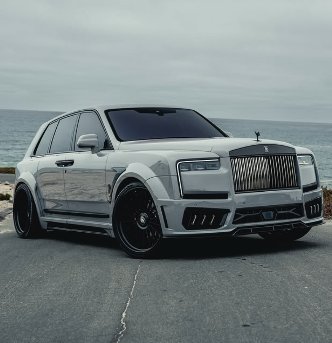 A silver luxury SUV parked on a coastal road with an ocean in the background.