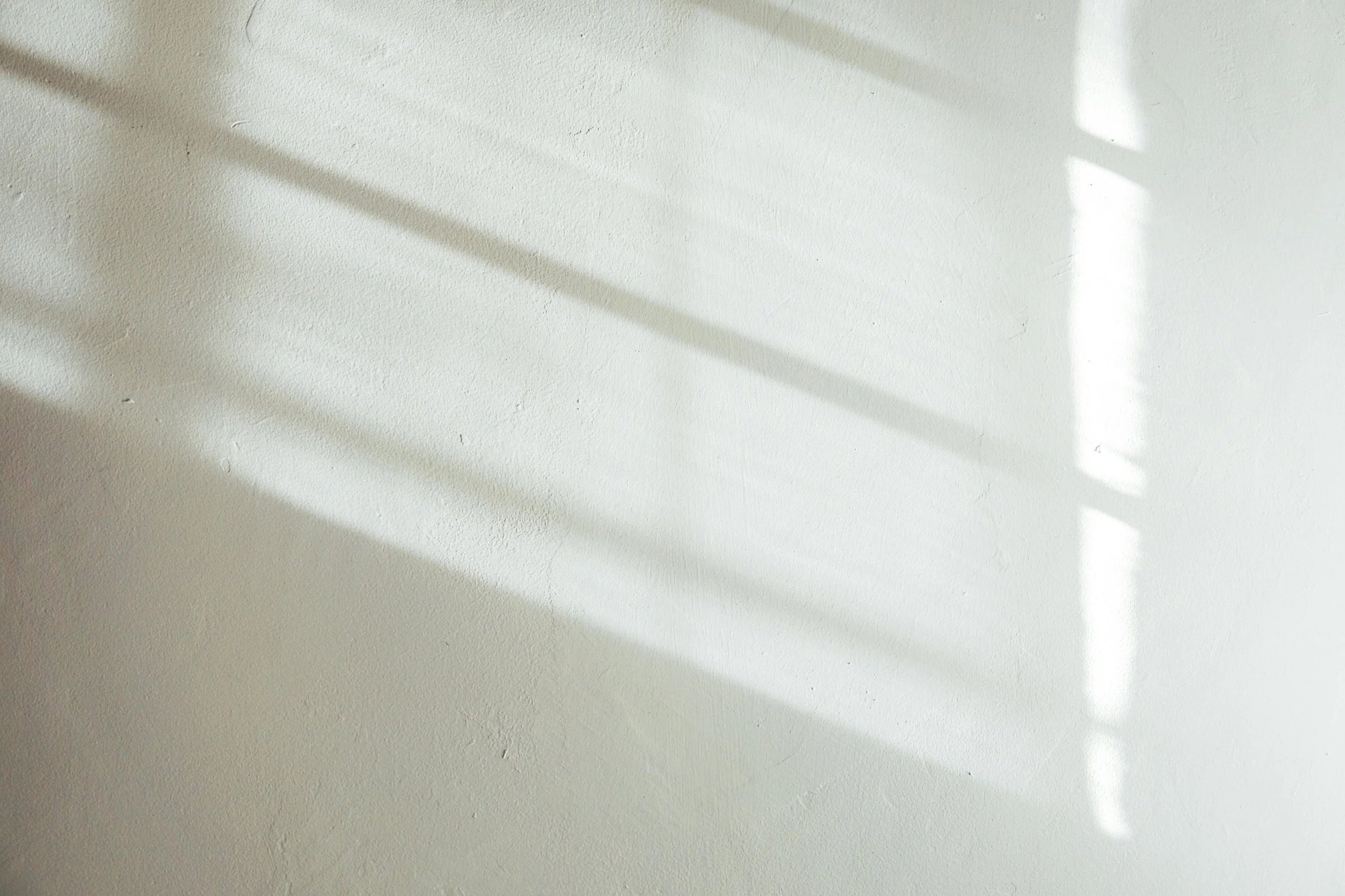 Shadows cast on a white textured wall, possibly from nearby window blinds.