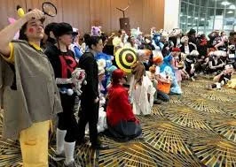 Group of people, including children and adults, dressed in costumes, attending a cosplay or costume event in a conference room with a patterned carpet.