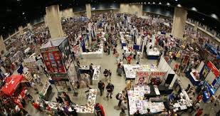 A crowded convention or trade show with numerous booths and attendees browsing.