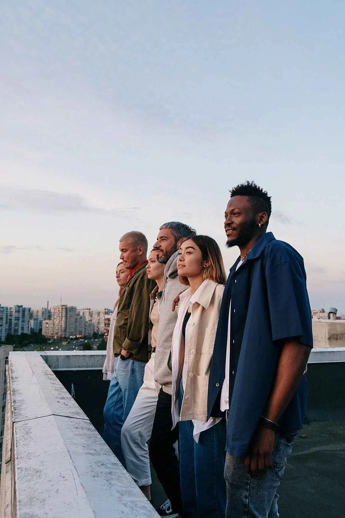 diverse group of people standing on rooftop watching the sunset