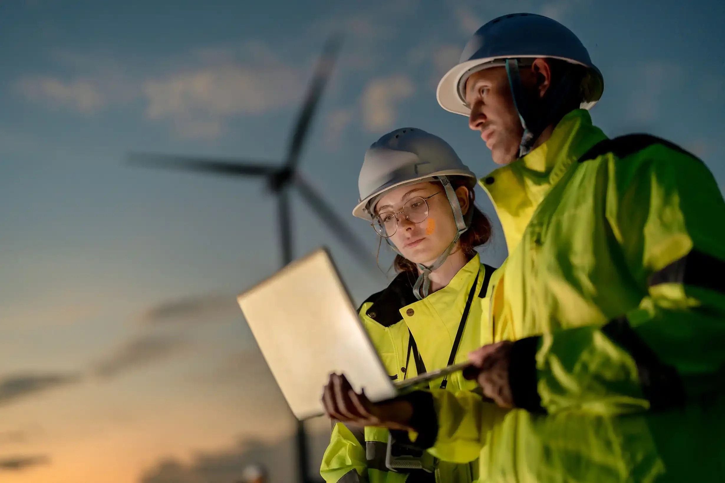 two workers analysing data on laptop during shift at wind energy plant, climate and energy software