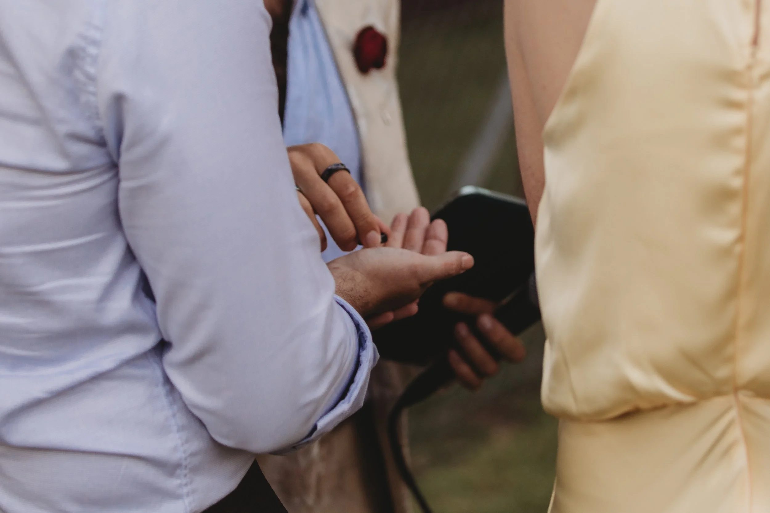Close-up of two people holding hands, one with a black ring and the other with long fingers.