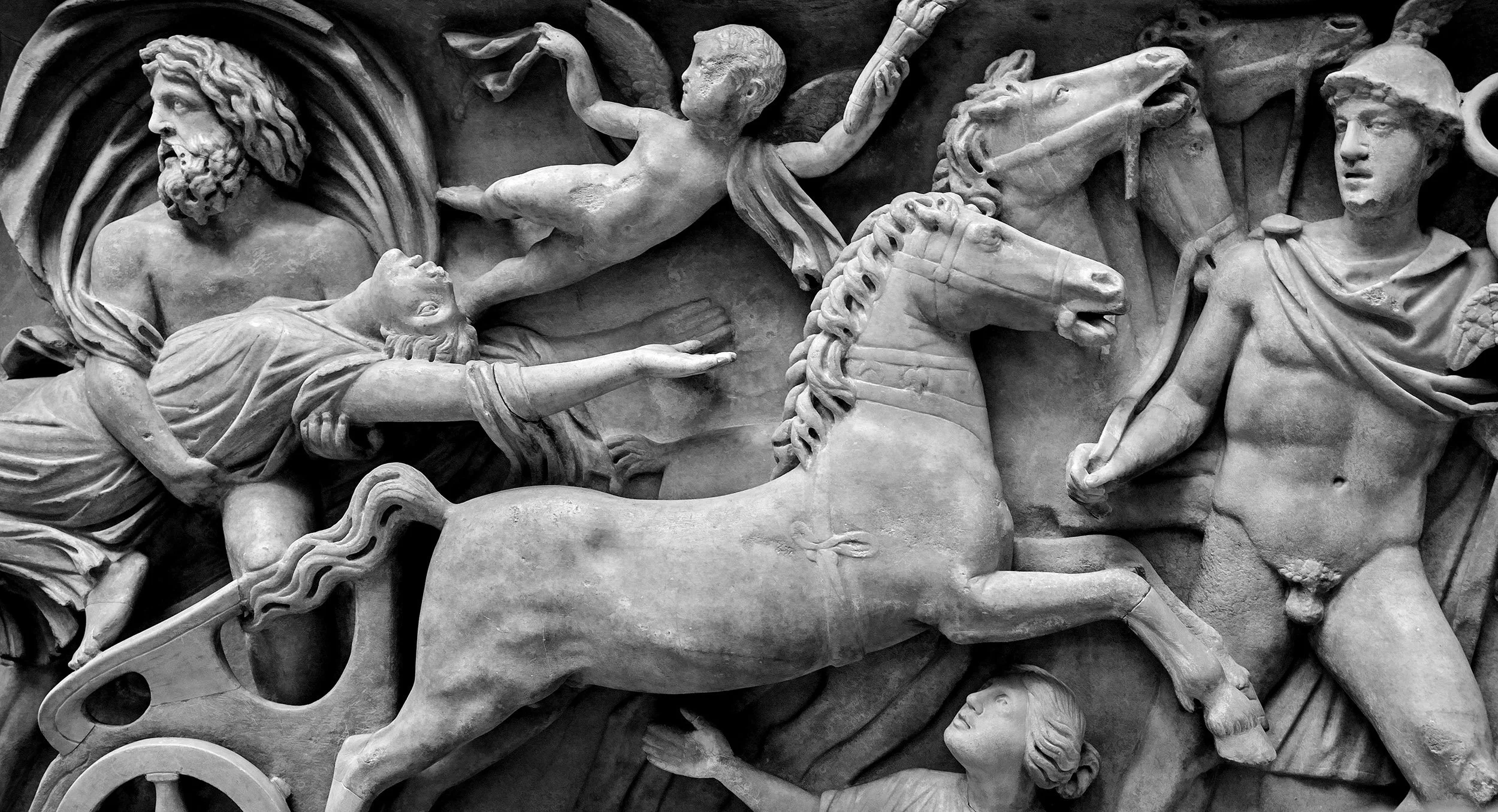 A detailed stone relief sculpture depicting a mythological scene with figures, horses, and expressive faces in a classical style.