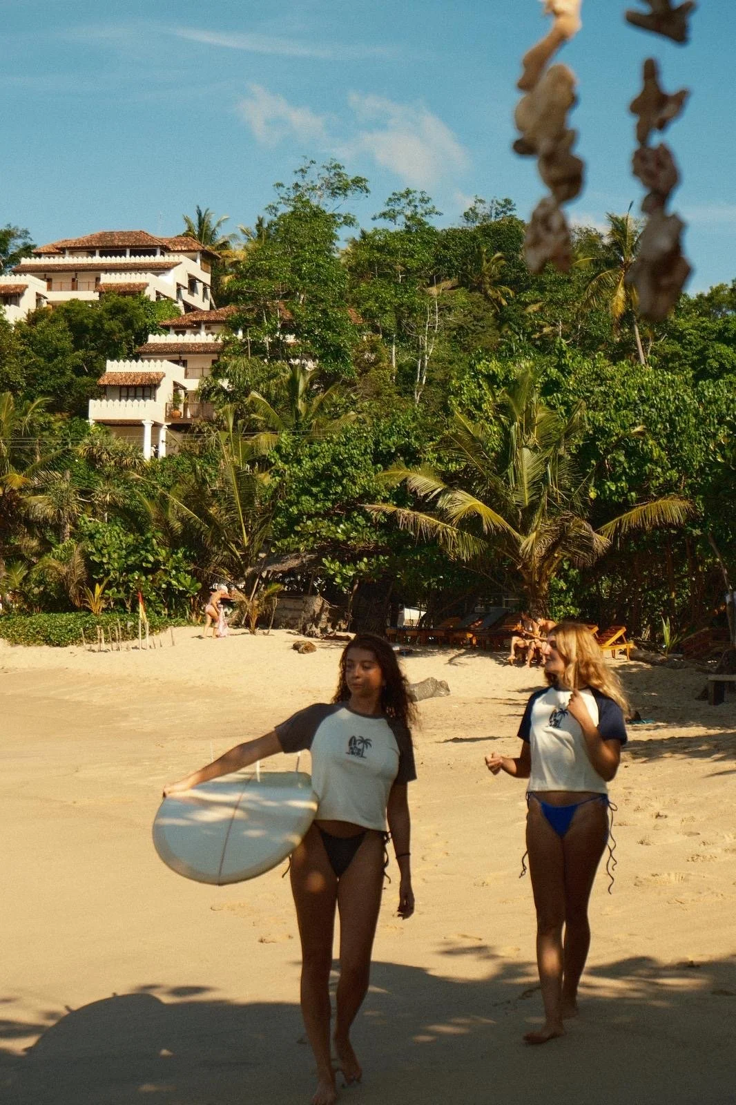Two women walking along the beach carrying surfboards during the Sorelle women’s surf and Pilates retreat in Sri Lanka.