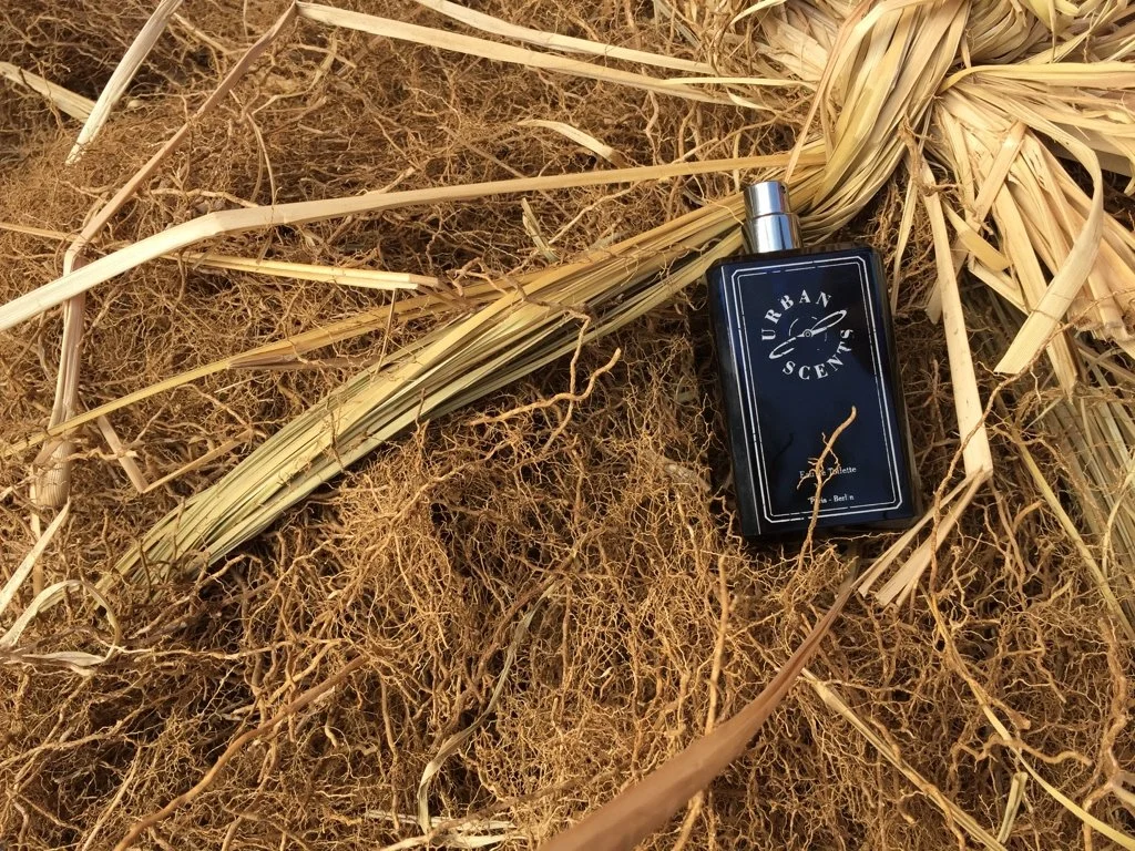 Black perfume bottle labeled 'Urban Scents' lies on dry grass and straw.
