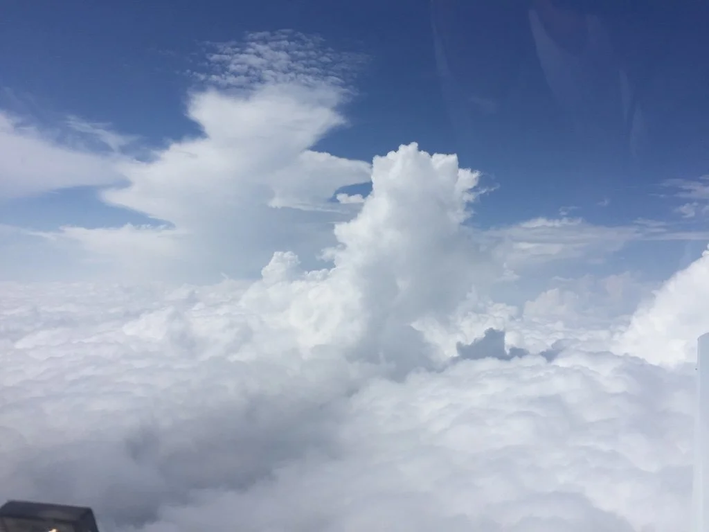 View of the sky with white clouds and patches of blue, taken from an airplane window.