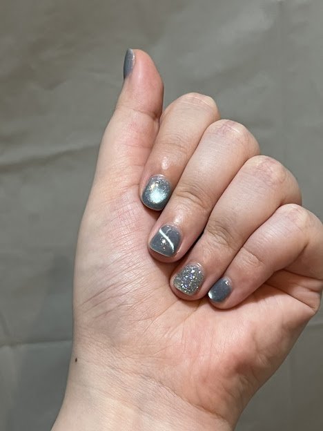 Close-up of a hand with glittery silver and gray nail polish on manicured nails.