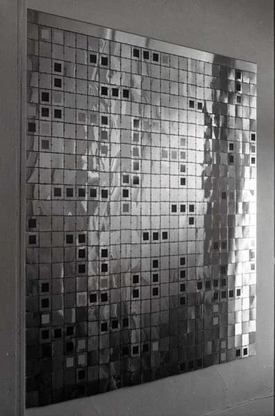 A wall of small reflective tiles arranged in a grid pattern, creating a mosaic effect.