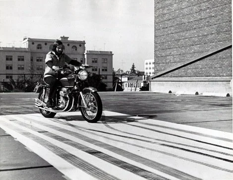 Person riding a motorcycle on a rooftop parking lot with buildings in the background