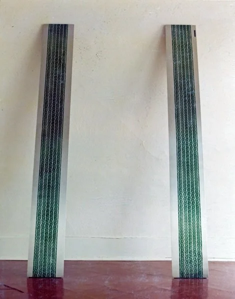 Two tall, narrow, vertical metallic panels with a green patterned design, standing against a plain beige wall.