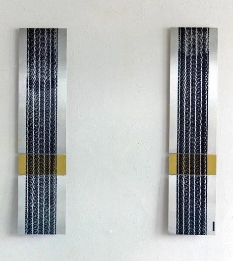 Two vertically oriented artworks with intricate blue patterns, each with a yellow block in the middle, mounted side by side on a plain white wall.