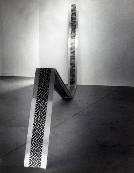 Abstract black and white patterned sculpture in a gallery space, with parts intersecting and extending vertically and diagonally.