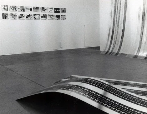Gallery with black and white photographs on the wall and fabric with stripes on the floor.