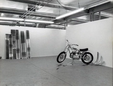 An indoor space with a motorcycle and four vertical metal racks against a white wall.