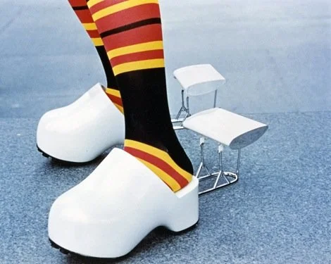Person wearing striped socks and large white shoes, sitting on a small clear chair.