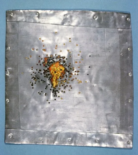 A metal shooting target with a burnt piece of bread and bullet holes.