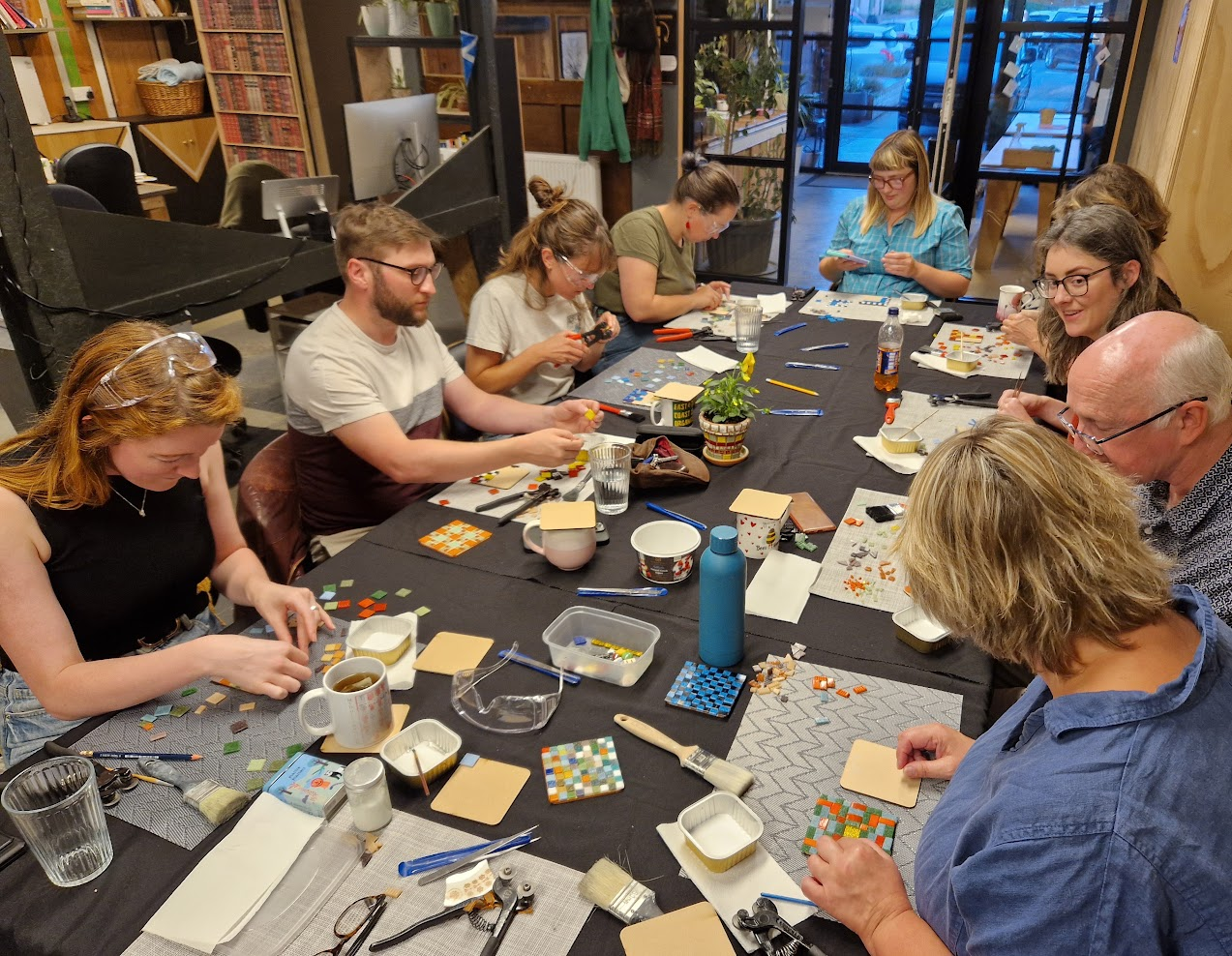 A group of people sitting around a table working on mosaic craft projects in a cozy room with wooden walls and glass doors.