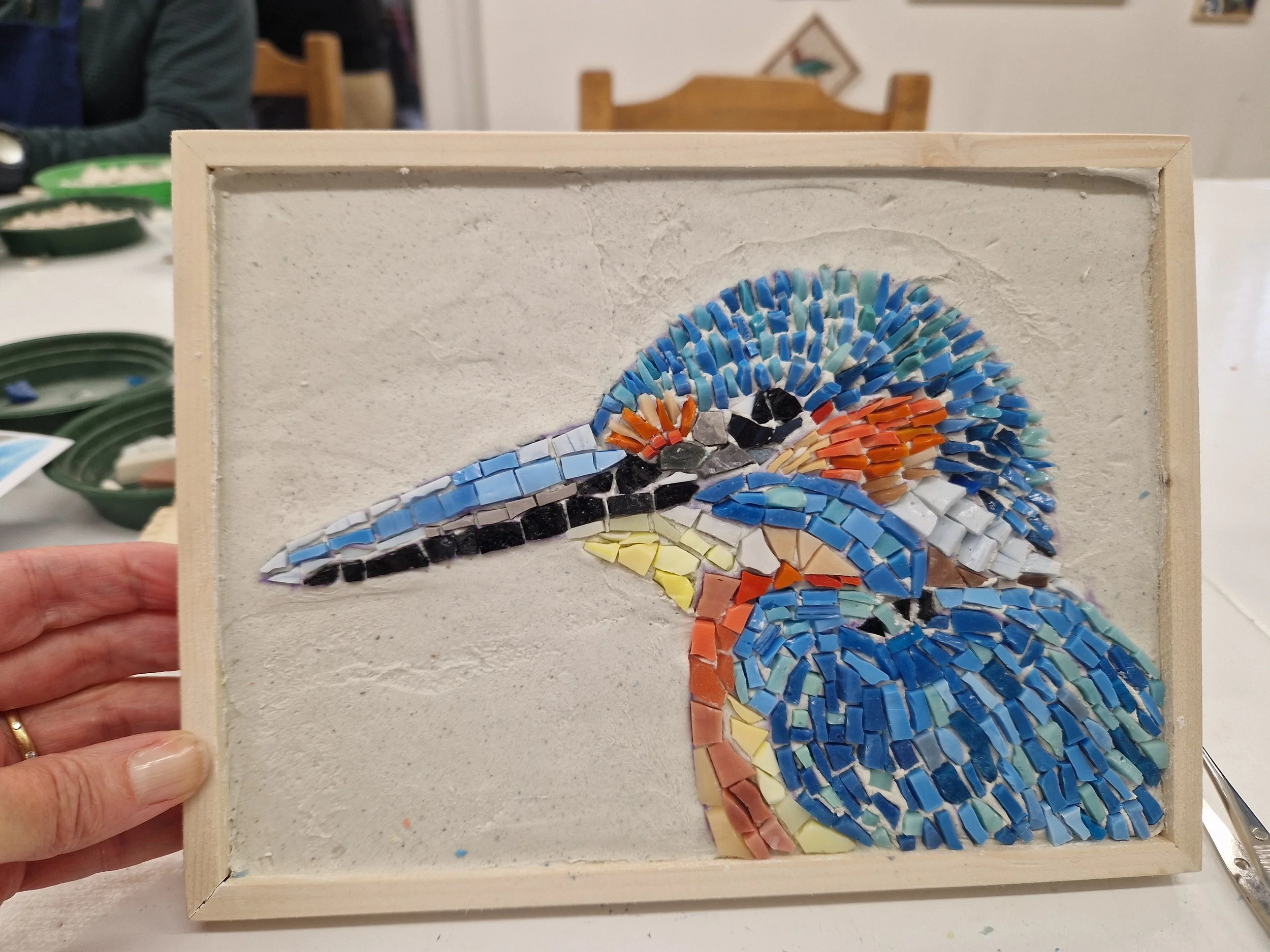 An intricate, framed, mosaic piece of a colourful blue, orange and white bird.
