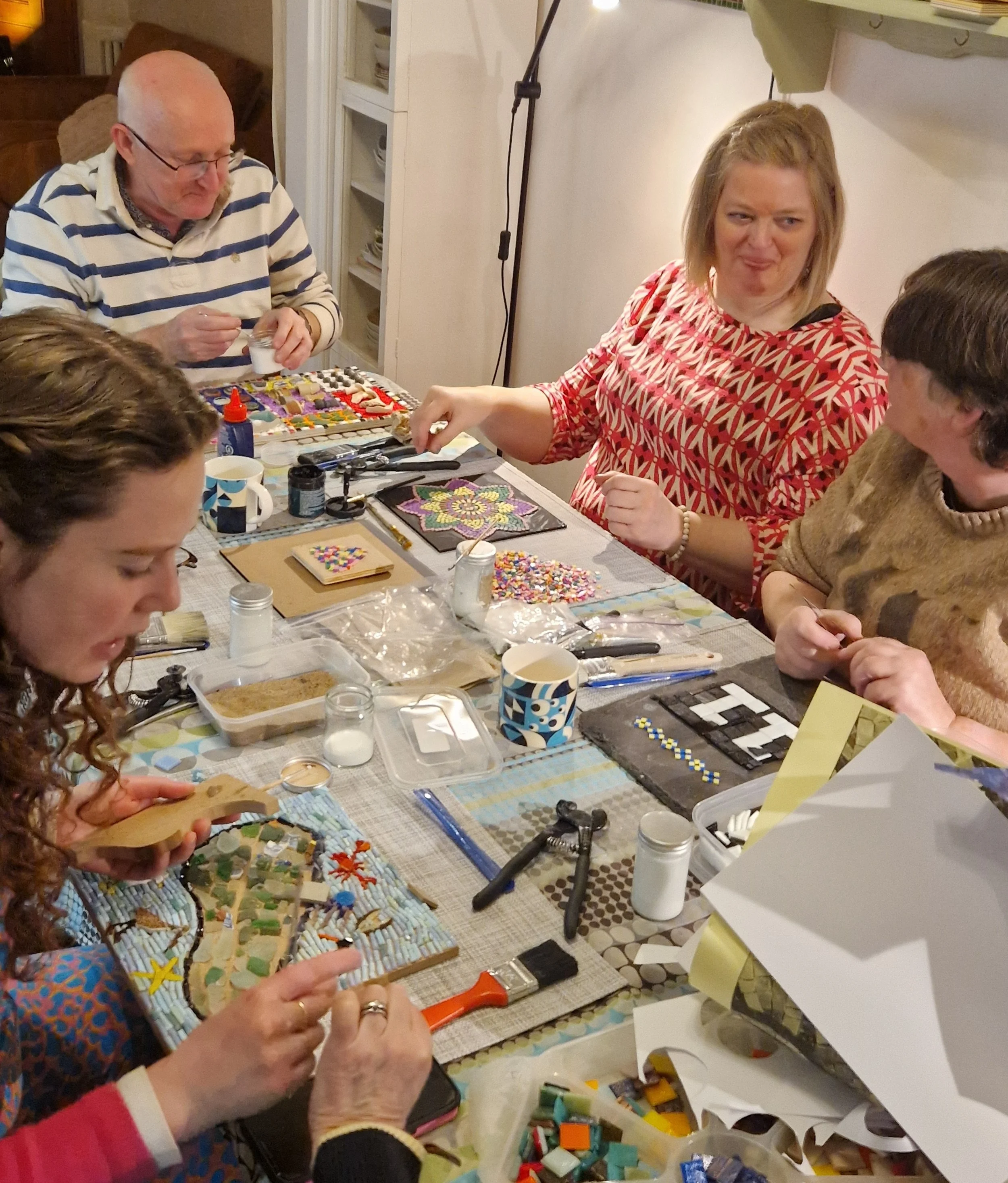 People creating mosaic art with colorful tiles on a table.