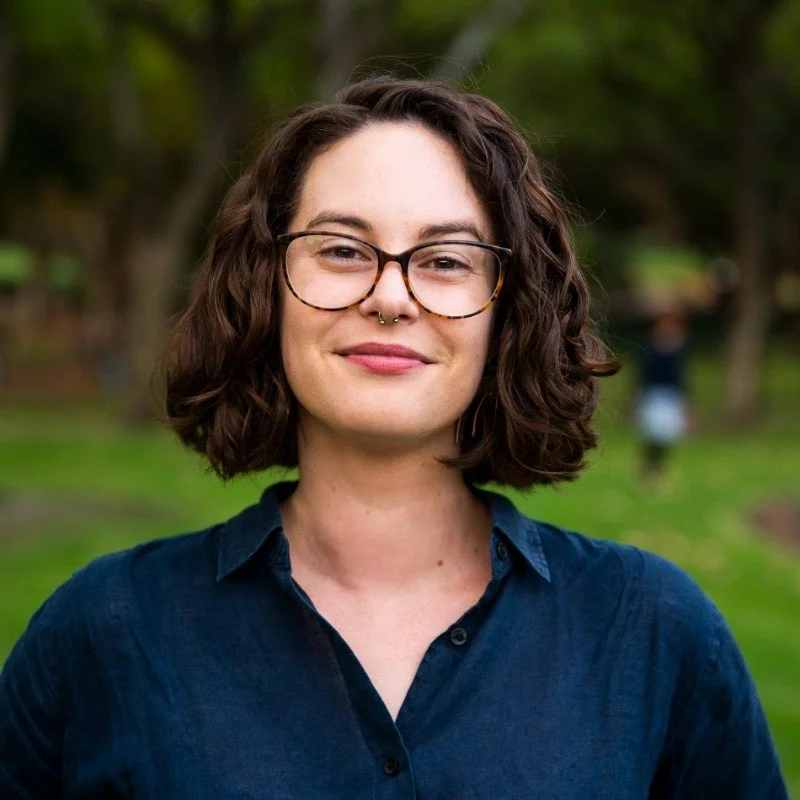 A woman with brown curly hair and glasses smiles at the camera