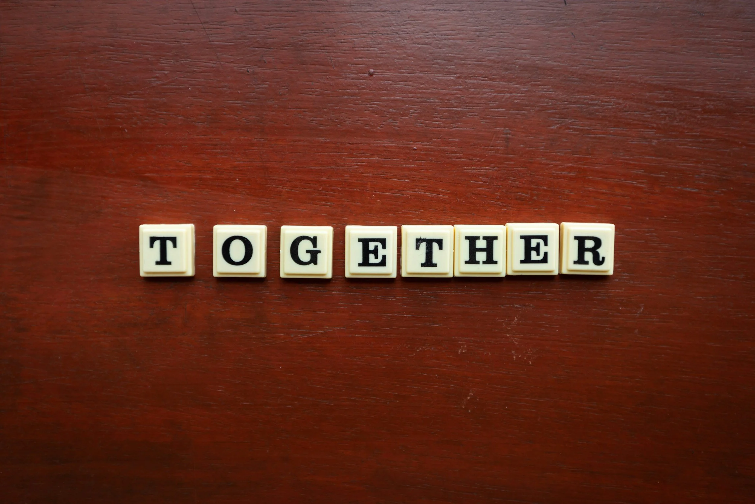 Scrabble tiles spelling the word "Together" on a wooden surface.