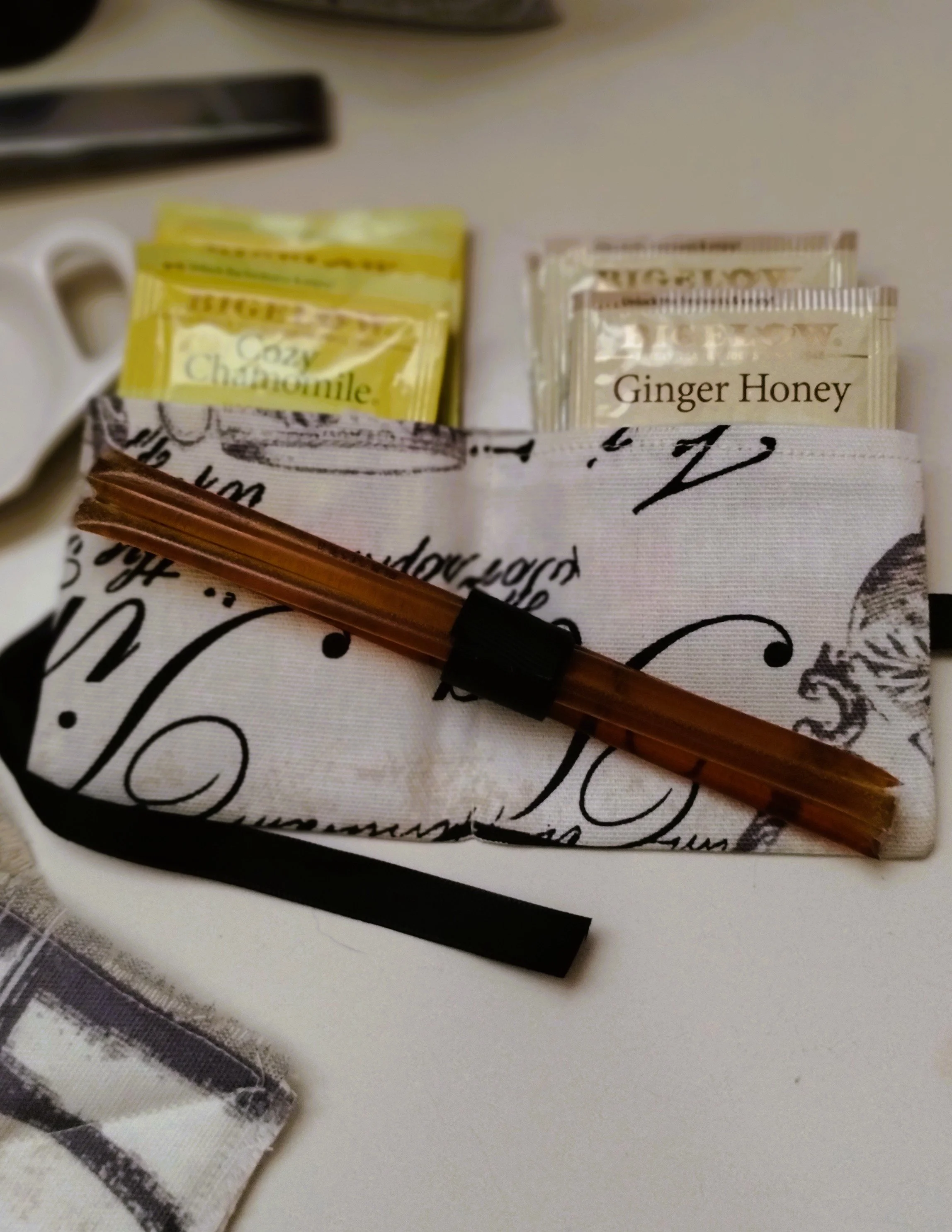 Chamomile and ginger honey tea with honey sticks in a handmade black and cream fabric holder.