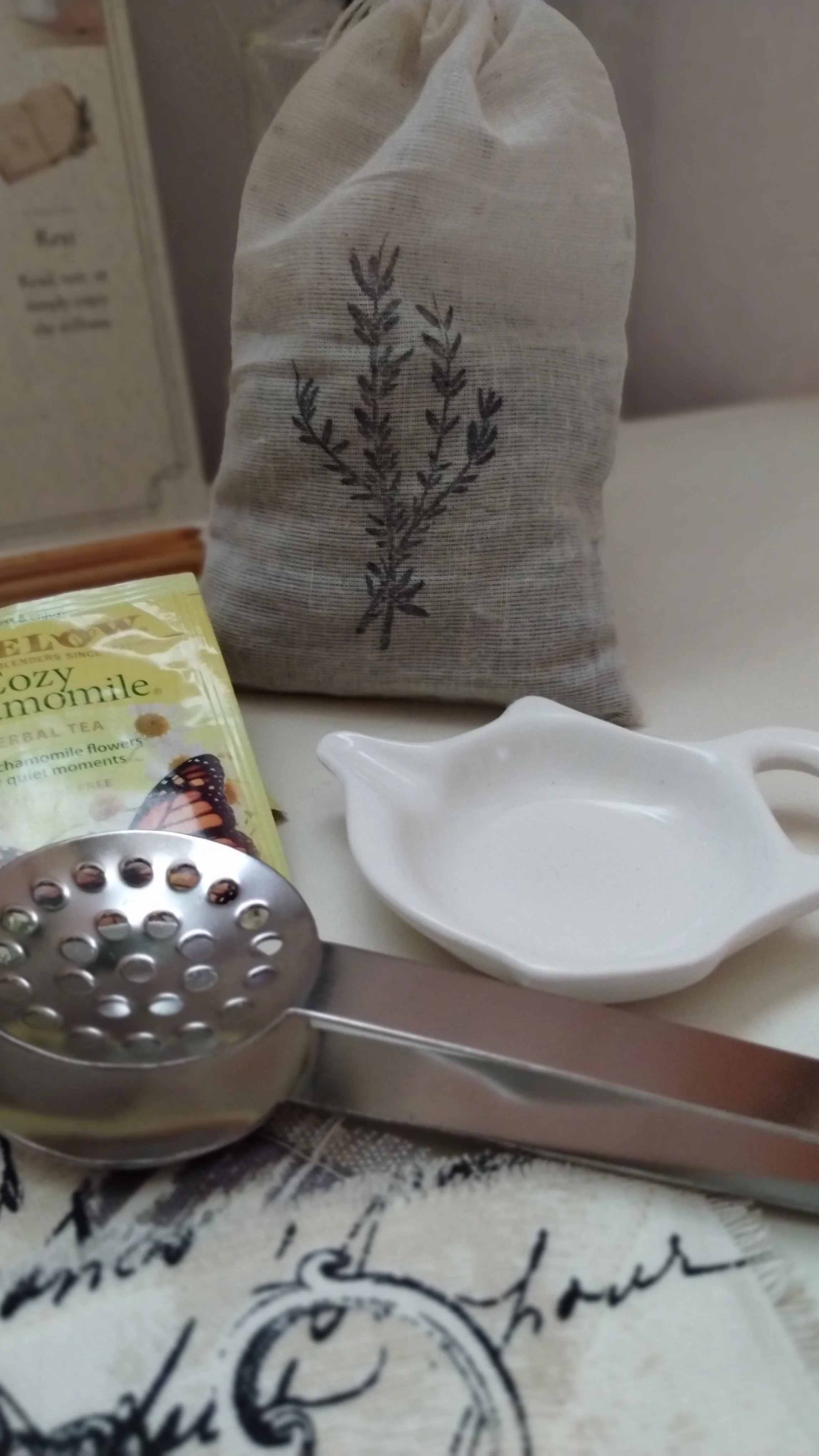 White ceramic tea bag rest and metal tea squeezer displayed beside herbal tea and lavender sachet.