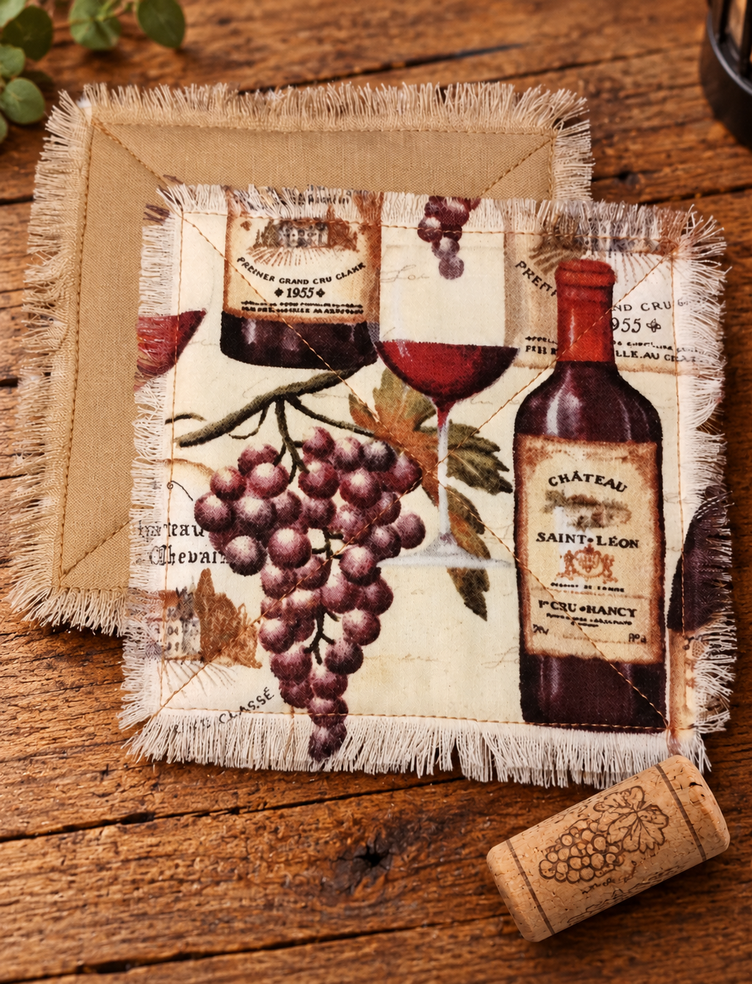 Handmade fabric coasters featuring wine bottles, grapes, and vintage vineyard labels, with natural cotton backing, quilted stitching, and fringed edges beside a wine cork.