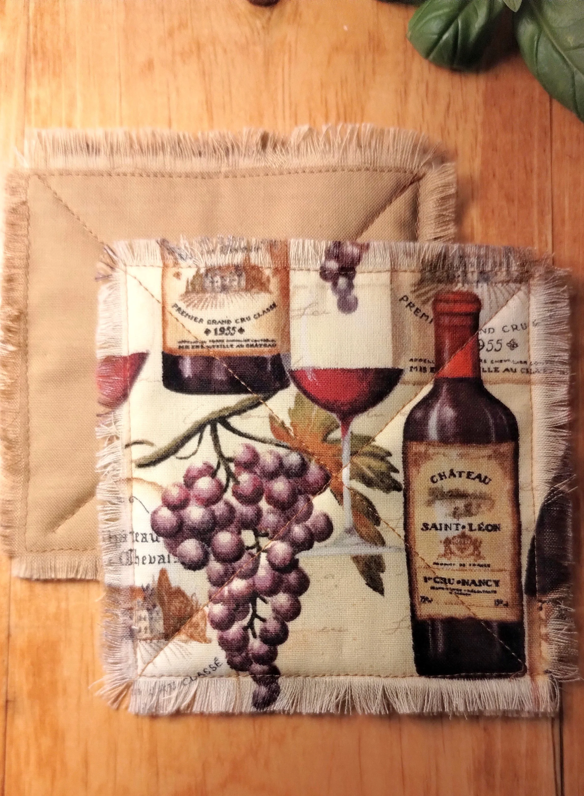Handmade fabric coasters featuring a vintage wine bottle and grape print in burgundy and cream, with X-stitch quilting and frayed edges.