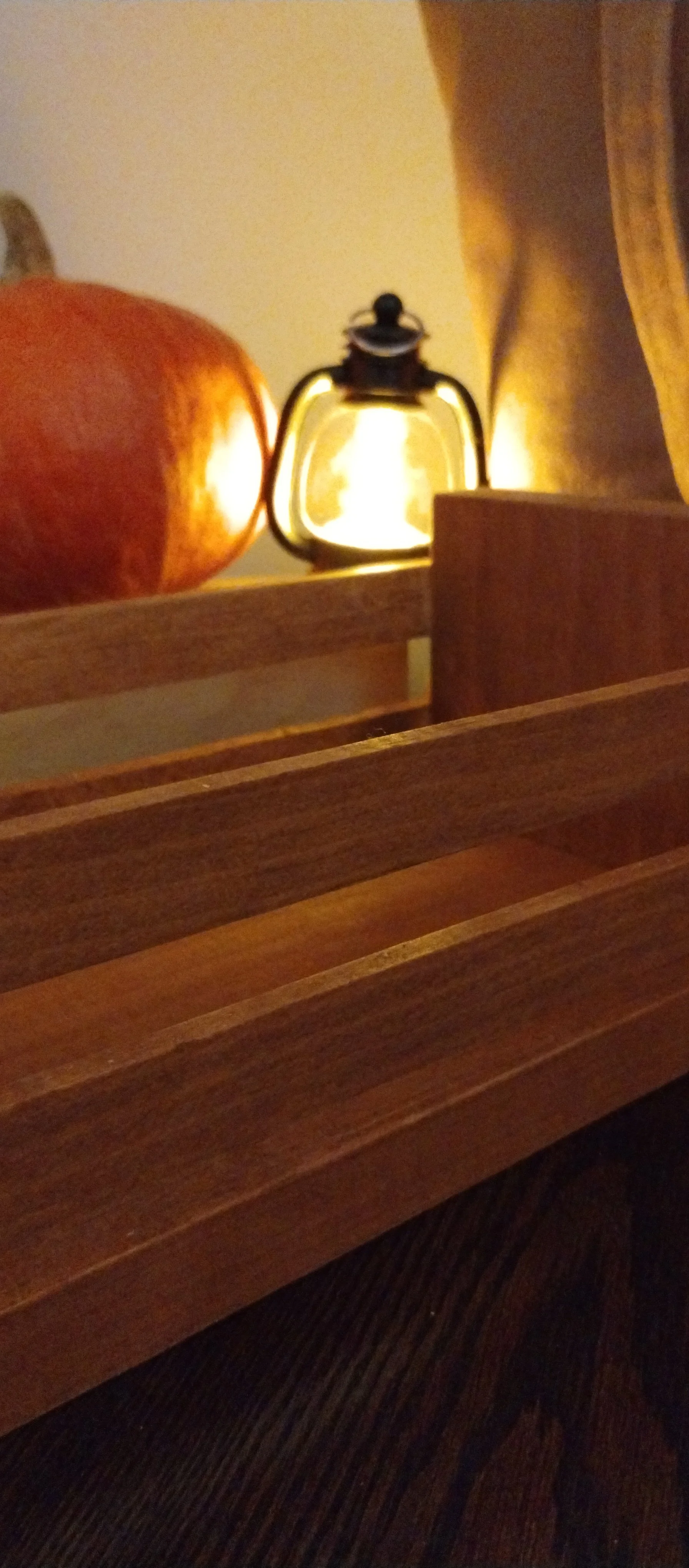 Close-up of warm stained wooden slatted crate with glowing mini lantern and pumpkin in a softly lit autumn setting.
