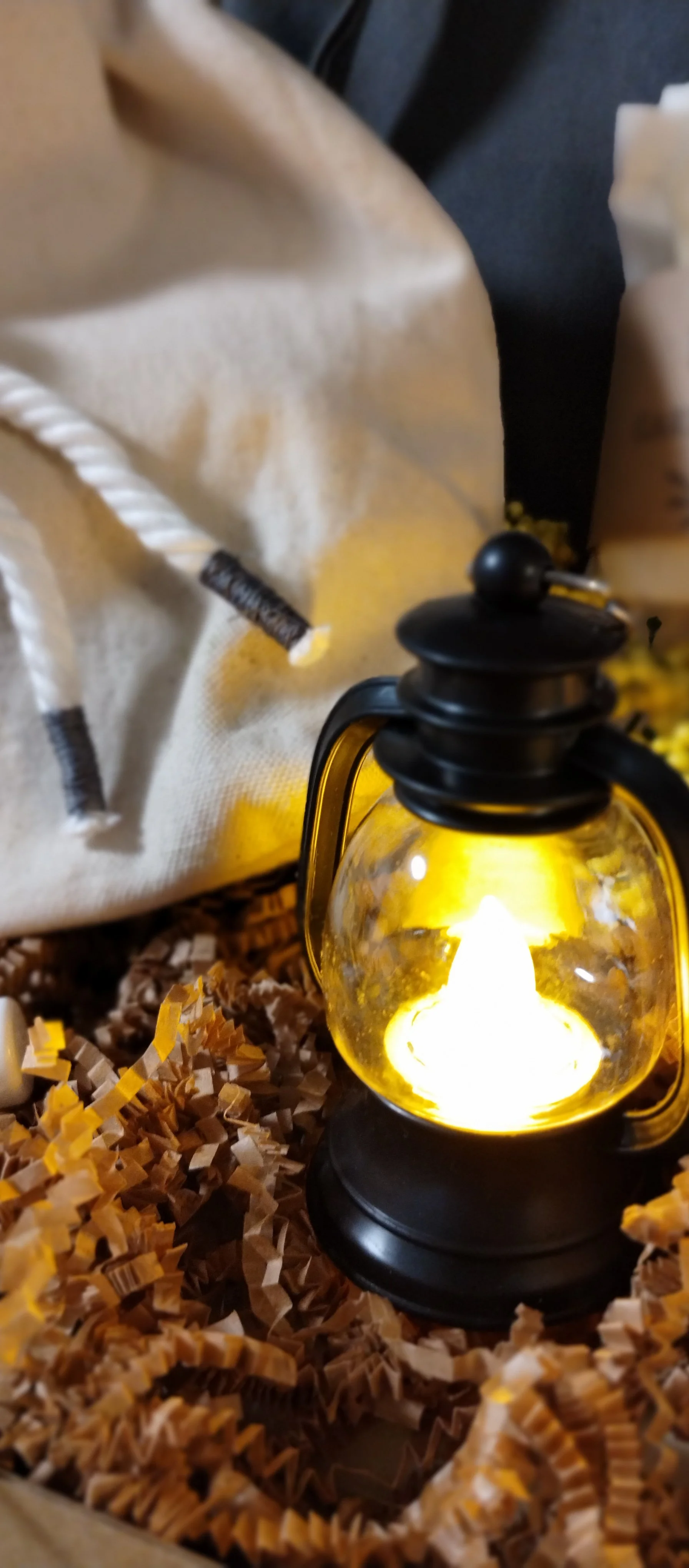 Close-up of glowing black mini lantern nestled in kraft paper beside the handmade canvas gathering pouch.