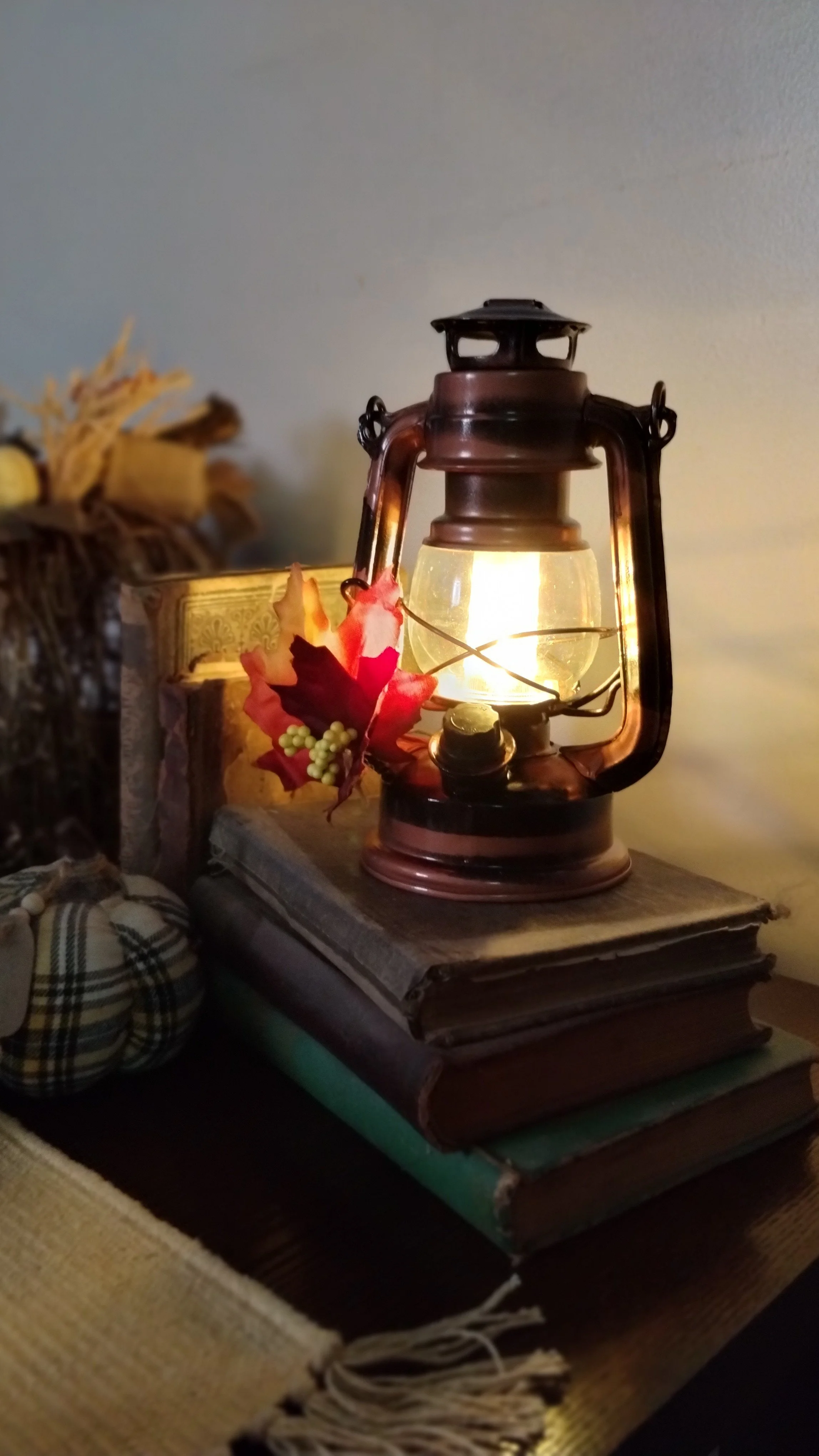 Lantern on old books: Glowing lantern decorated with fall leaves and displayed on a stack of vintage books with fabric pumpkins nearby.