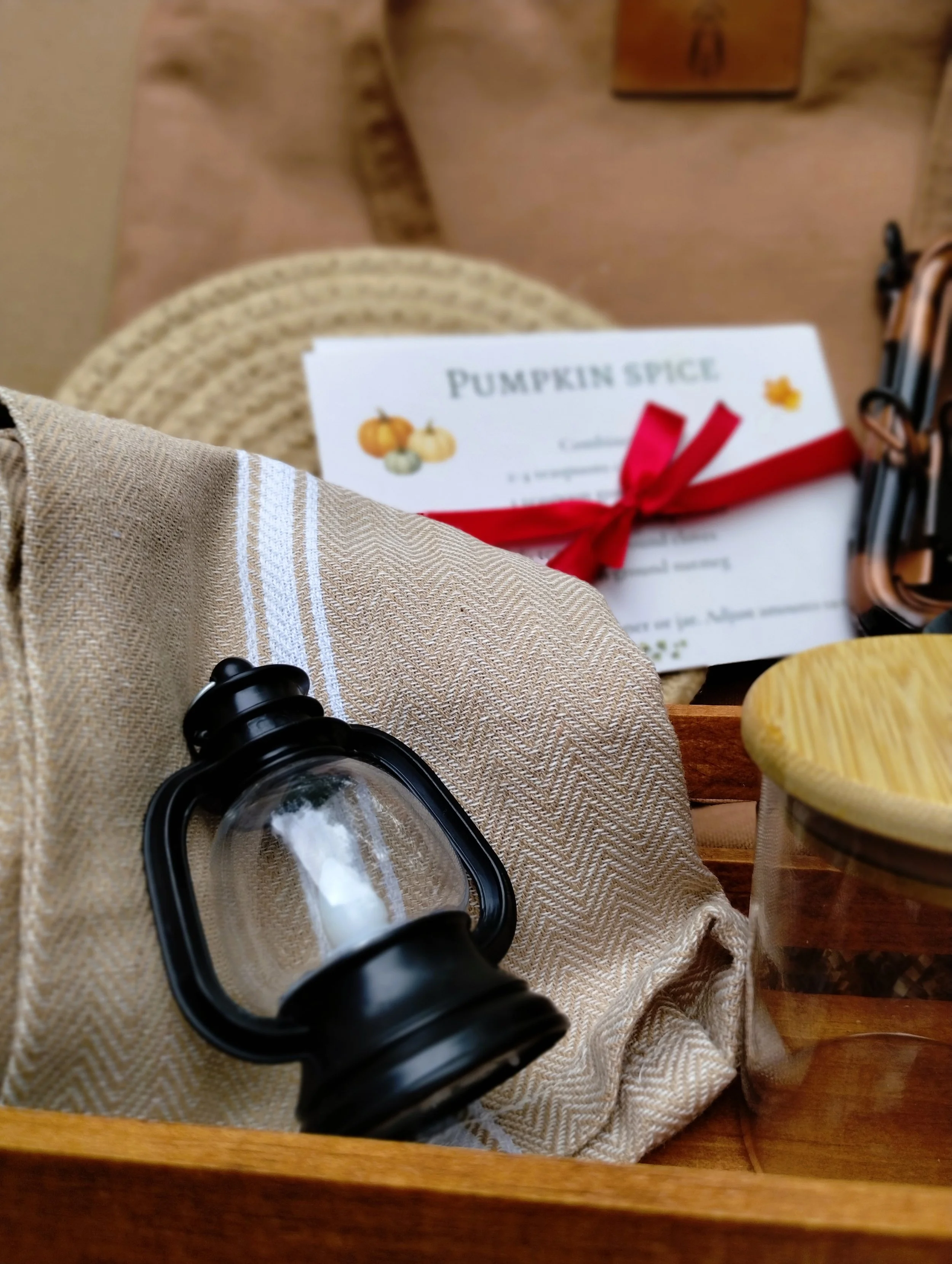 Wooden crate filled beige braided trivet, beige kitchen towel, mini lantern spice jar with wood lid, and spice recipe cards
