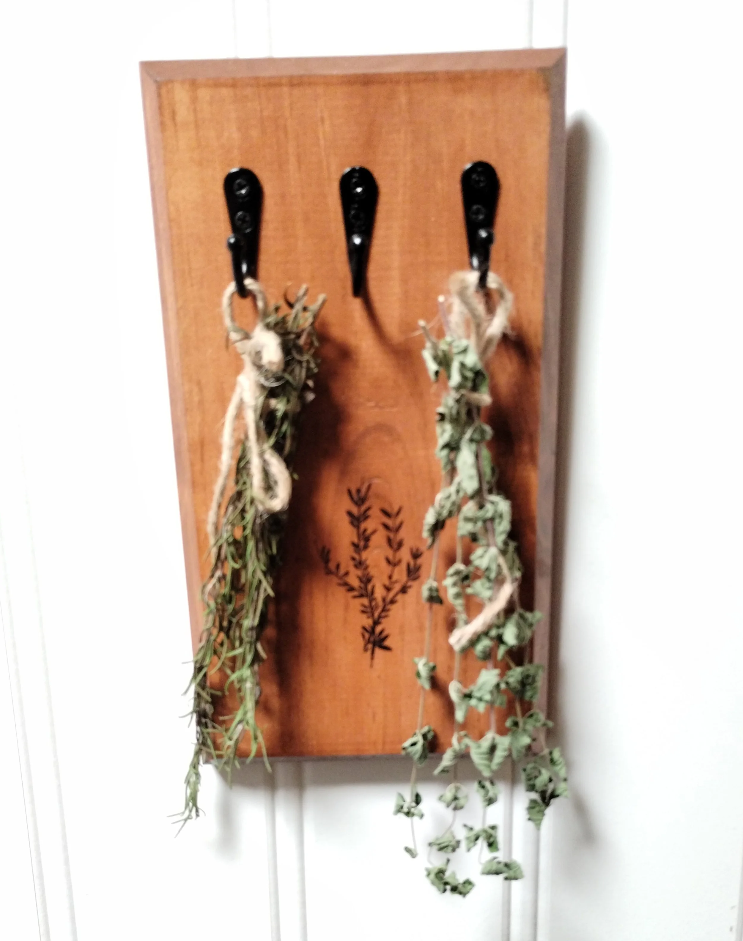 Wall-mounted herb drying rack with bundles of dried herbs hanging from black hooks