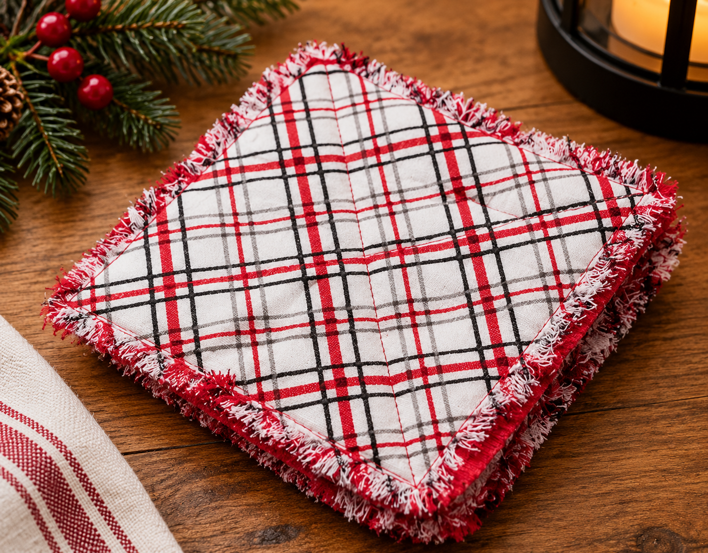 Handmade red, white, and black plaid fabric coasters with decorative stitching and frayed edges, displayed on a rustic wooden table.