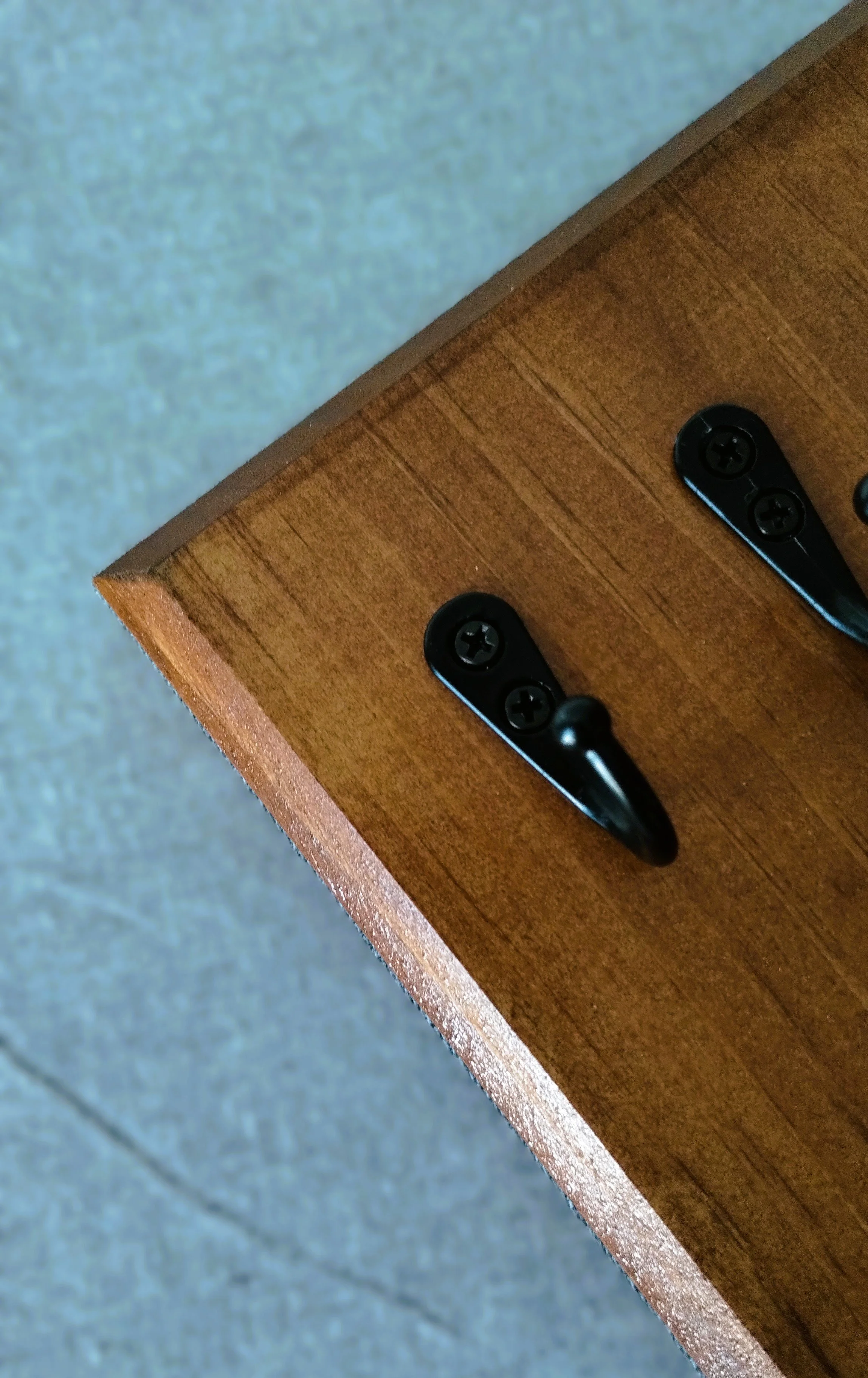 Close-up of black metal hooks and natural wood grain on handmade wall-mounted herb drying rack.