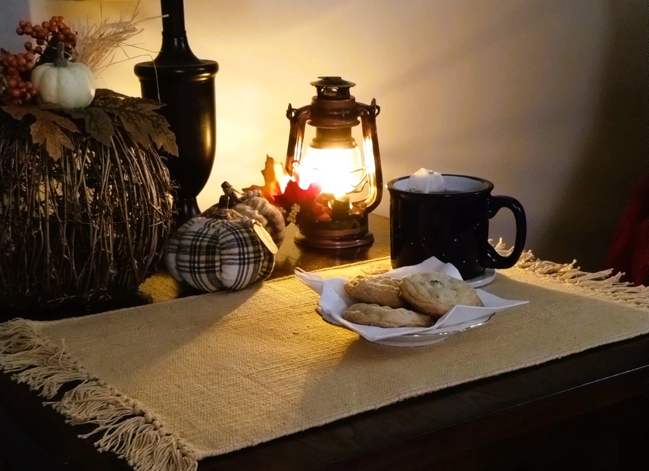 Cozy fall scene: Glowing lantern with fall pumpkins, a warm drink, and cookies arranged on a table for a cozy autumn setting.