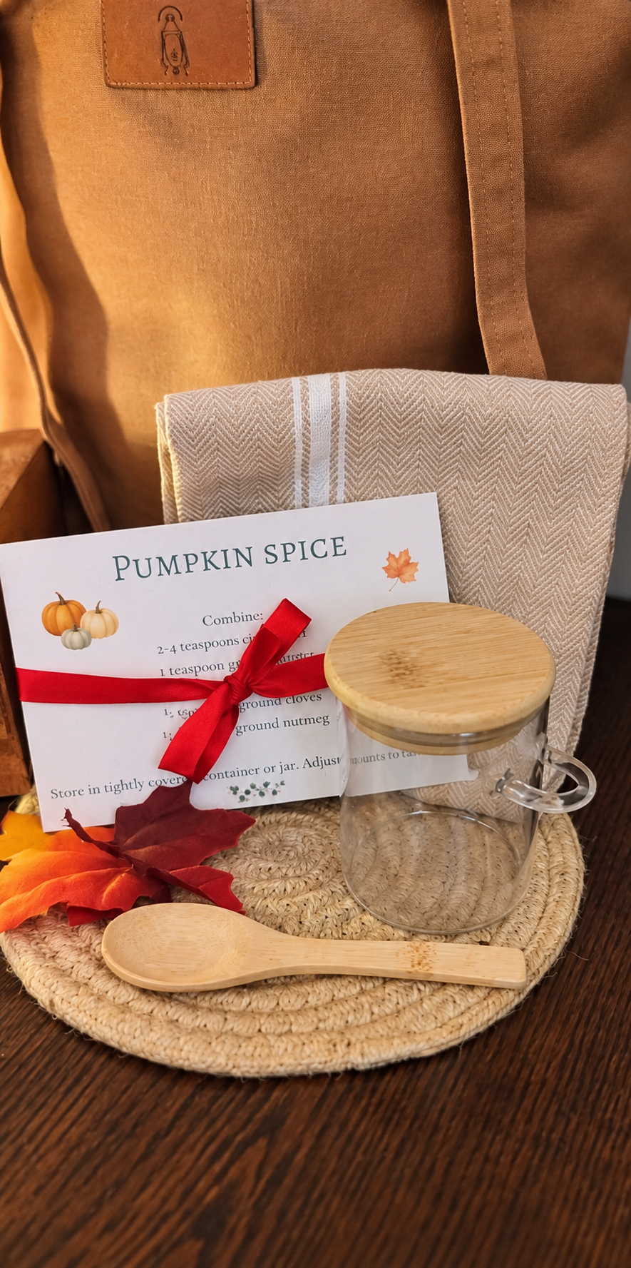 Pumpkin Spice recipe card with red ribbon, glass spice jar, wooden spoon, kitchen towel and braided trivet from the Autumn Afternoon Collection.