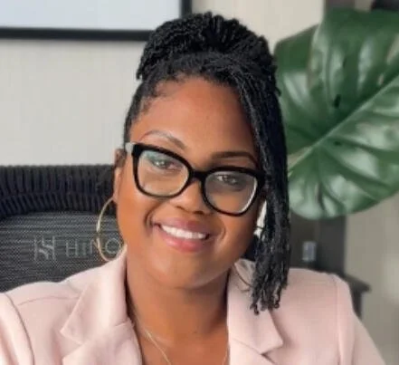 Kosi Nweke, a psychotherapist, Qualifying and student at York University working at Embrace Well Psychological Services. Smiling in a pink blazer in an office setting.