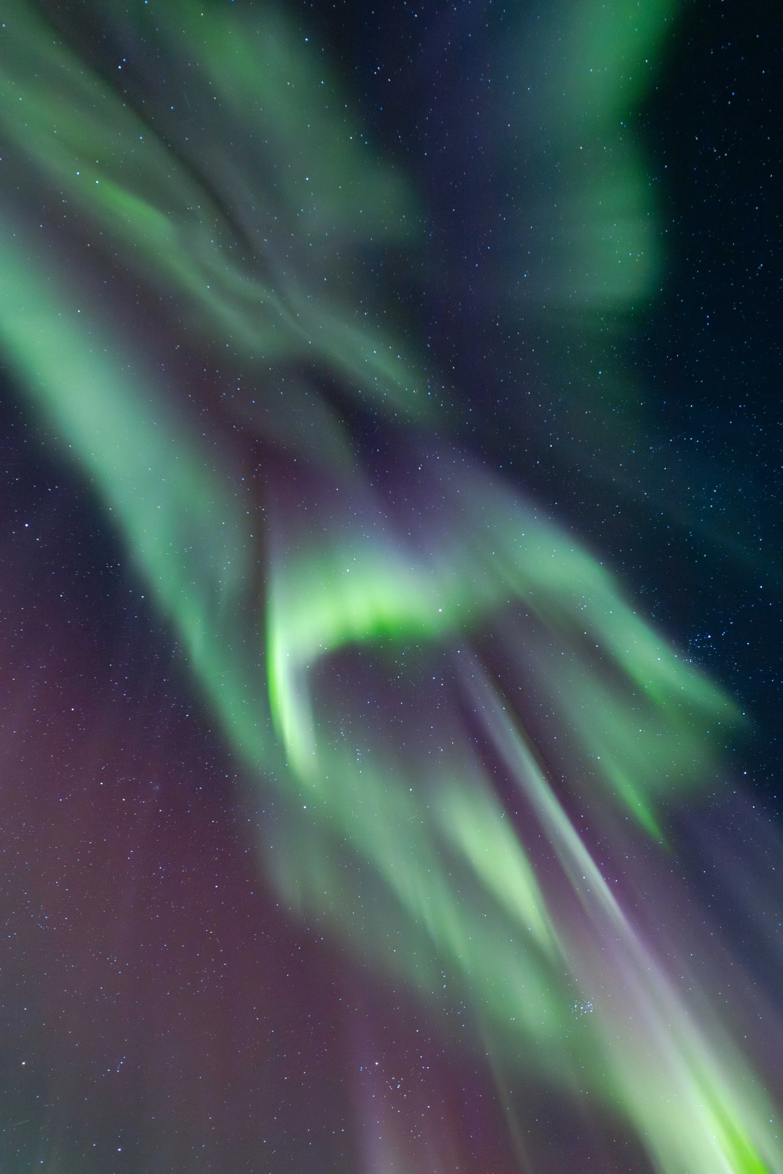 Imagen vertical de aurora boreal en movimiento, con formas abstractas y luces verdes atravesando un cielo nocturno estrellado en el Ártico noruego